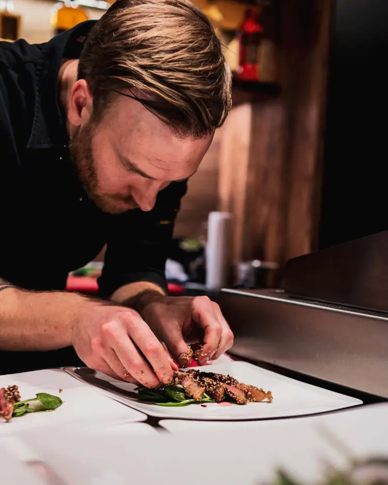 Privatkoch Sascha Zellinger richtet ein Gericht mit schwarzen Handschuhen an – Präzision beim Fine-Dining-Catering