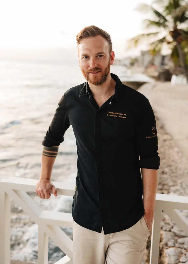 Privatkoch Sascha Zellinger in schwarzer Kochuniform am Meer – mobiler Privatkoch für Outdoor-Events